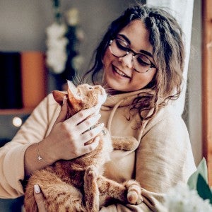 A woman holds a cat in her arms as they look lovingly at each other
