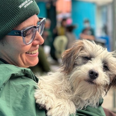 A dog is held by a smiling person in a green hat and jacket.