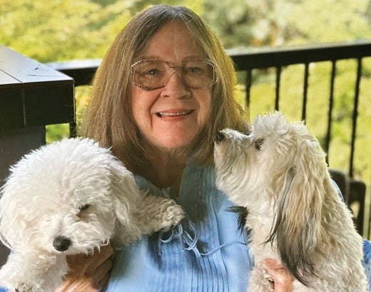 Woman sitting on a deck holding her two white dogs.