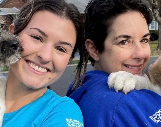 Two women are holding puppies and smiling at the camera