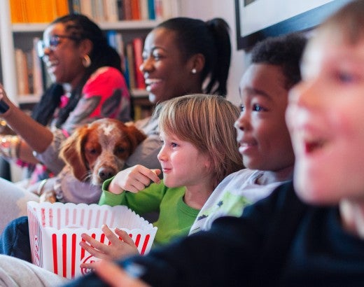 Multi-ethnic family watching movie and eating popcorn on the couch watching a movie with a dog.