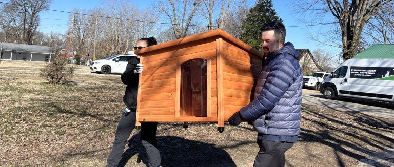 Two people carrying a doghouse