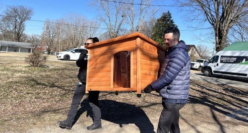 Two people carrying a doghouse