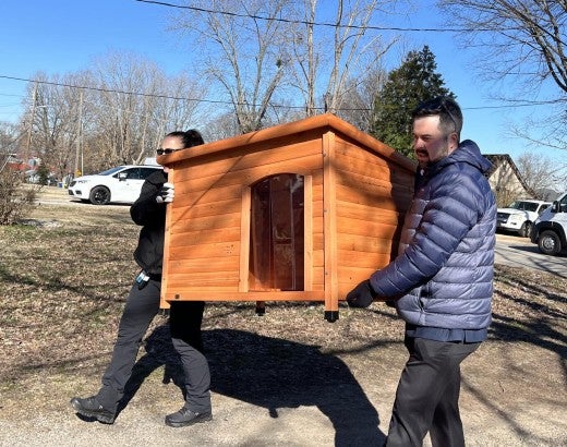 Two people carrying a doghouse