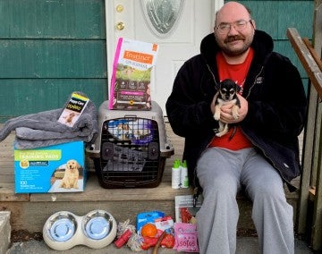 Man sitting with his new puppy sitting on his porch filled with pet supplies