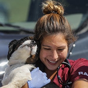 a RAVS volunteer laughs while the small dog she's holding nuzzles her face