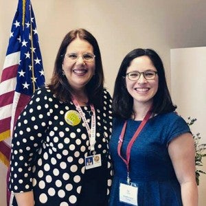 Two woman standing in front of American flag.